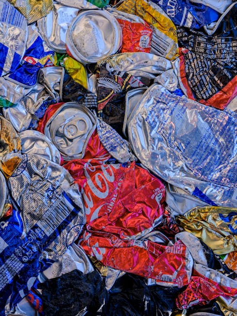 A black, cylindrical public trash bin with a domed lid, situated on a cobblestone pavement outdoors. The bin is surrounded by discarded items, including several glass bottles arranged at its base, som